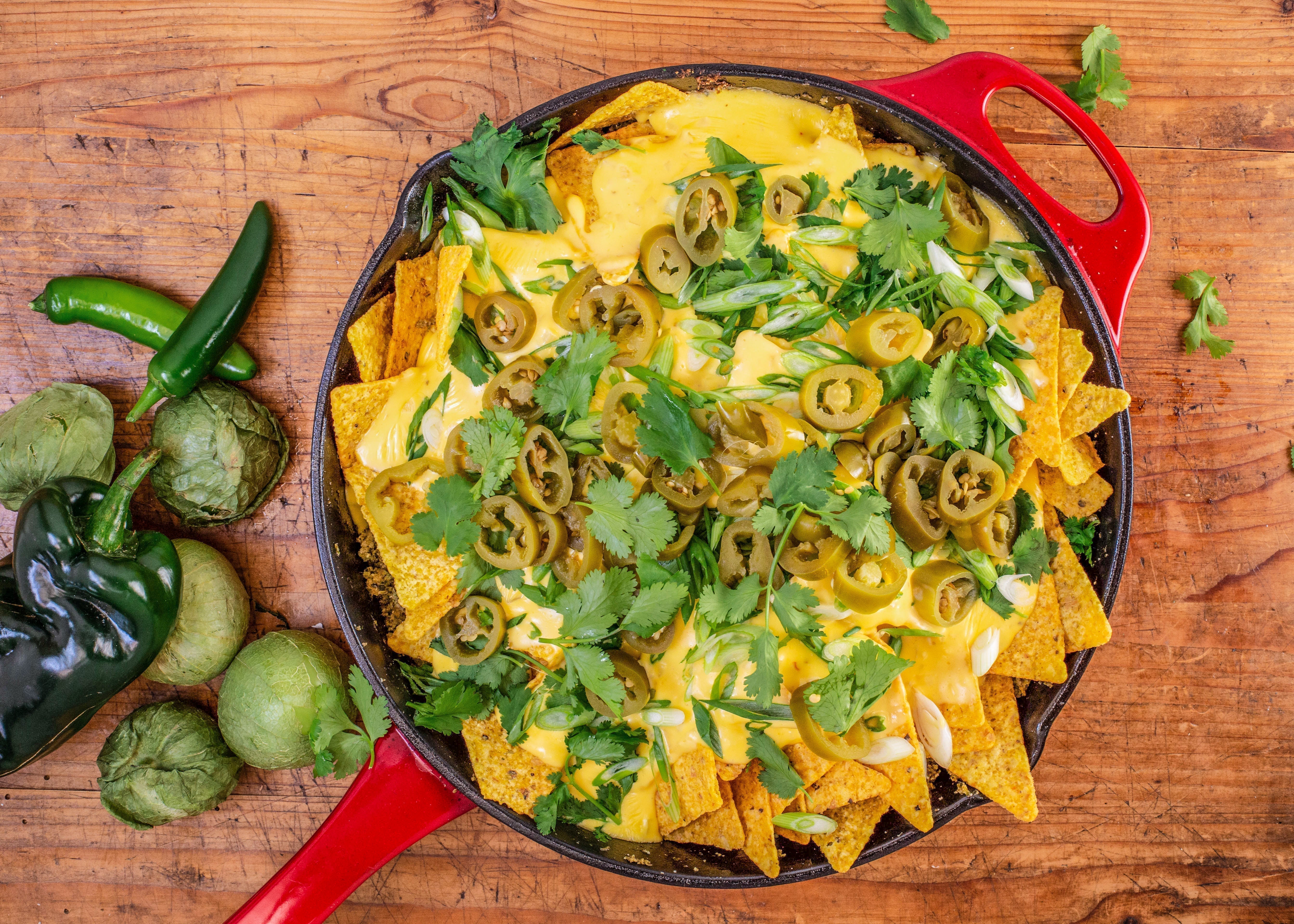 Cast Iron skillet full of green chorizo nachos covered in melted cheese, jalapeño slices and cilantro