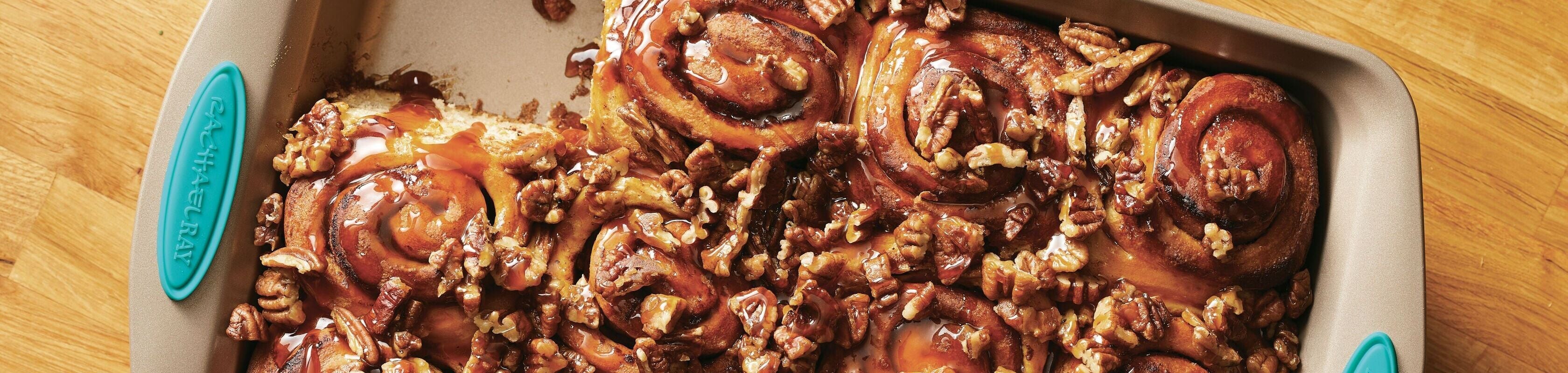 A baking pan filled with sticky caramel pecan cinnamon rolls sits on a wooden surface.