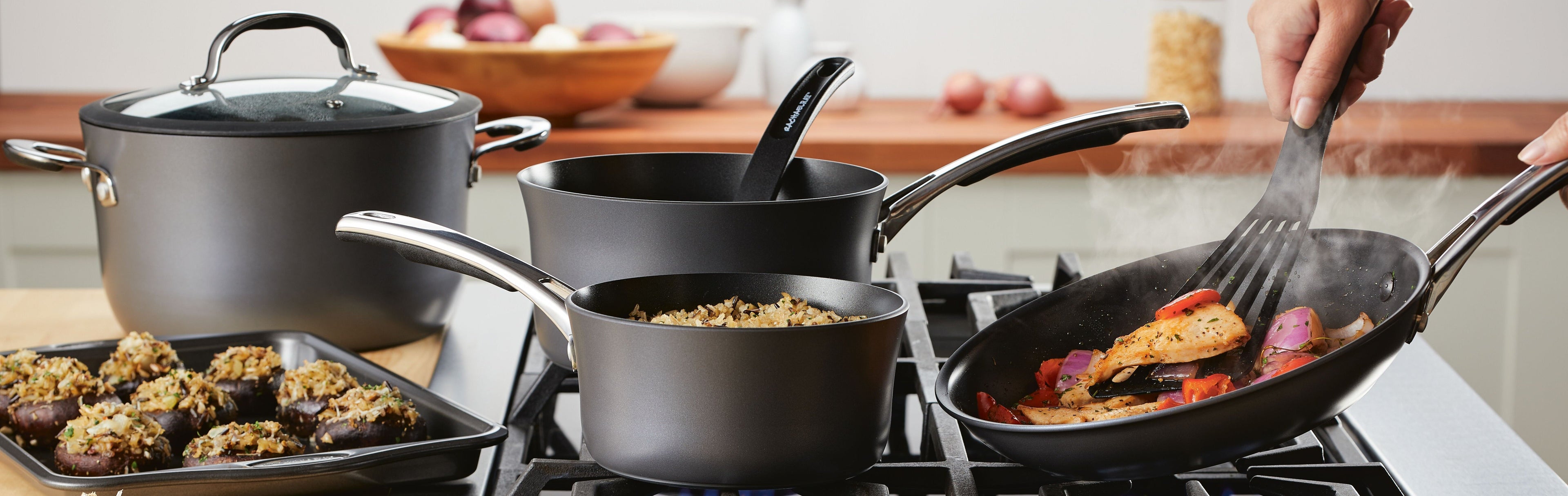 A woman cooks at a modern kitchen stove with blue cookware, surrounded by fresh ingredients, utensils, and bread on the counter.