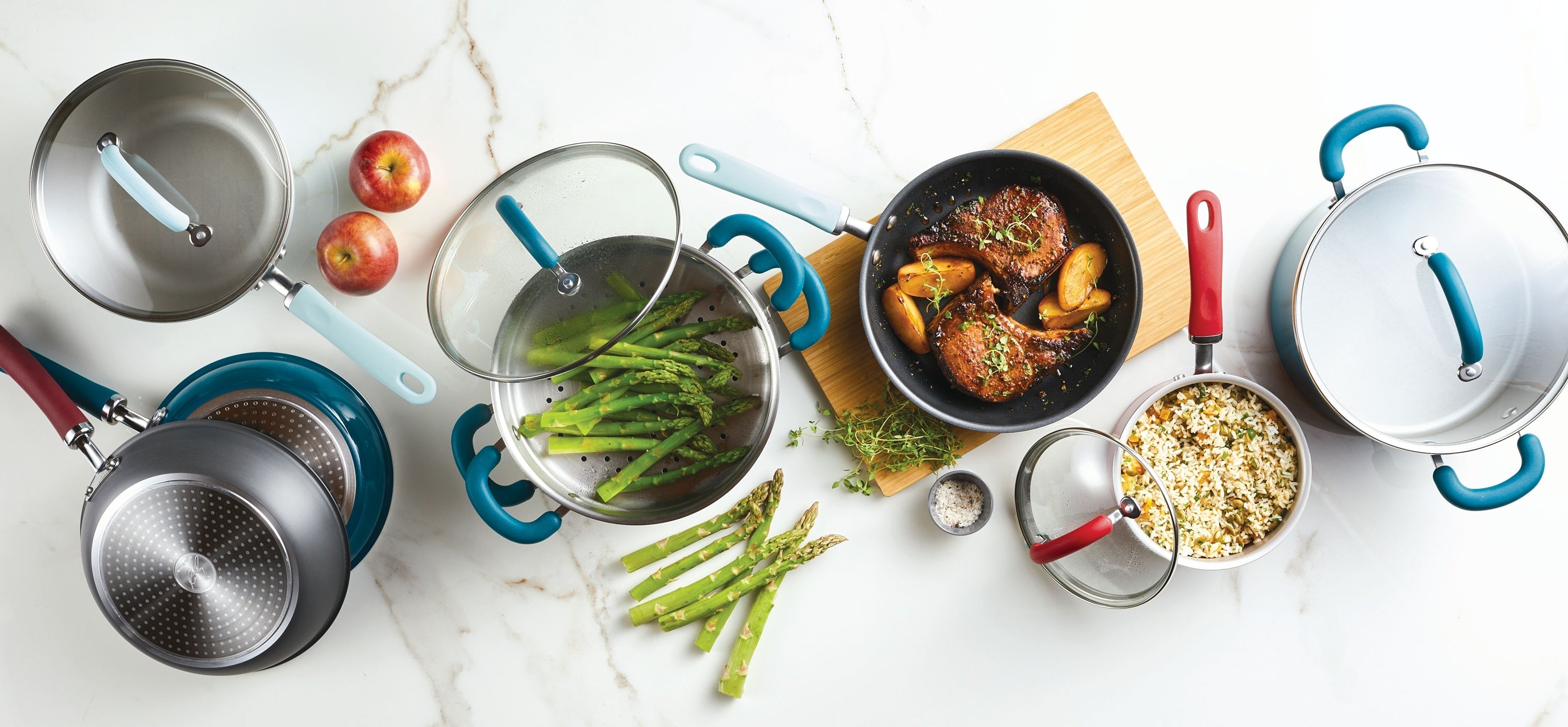 Person cooking on a stovetop with teal cookware, surrounded by various fresh vegetables and kitchen utensils on a marble countertop.
