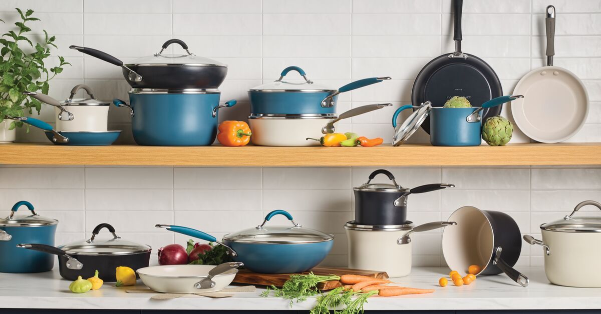 Assorted blue and white cookware sets displayed on wooden shelves with vegetables on a white countertop.