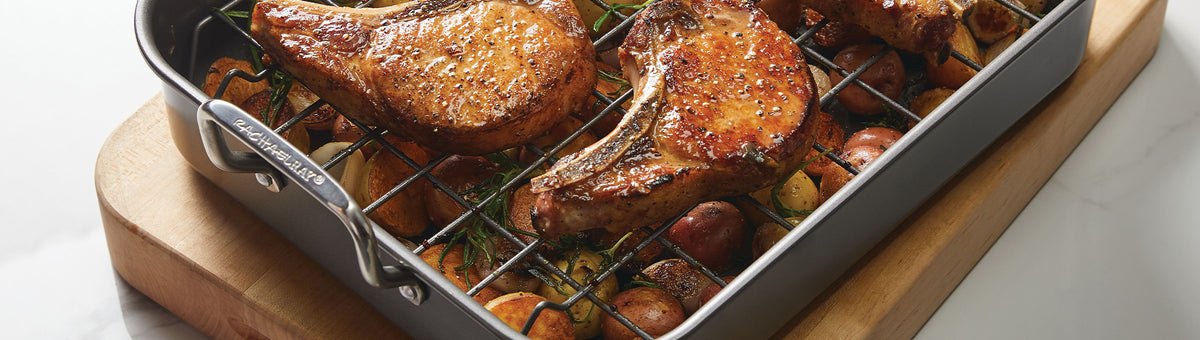 Grilled pork chops on a rack in a roasting pan, resting over a mix of roasted vegetables.