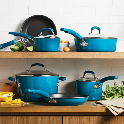 Teal cookware set displayed on wooden shelves with vegetables.