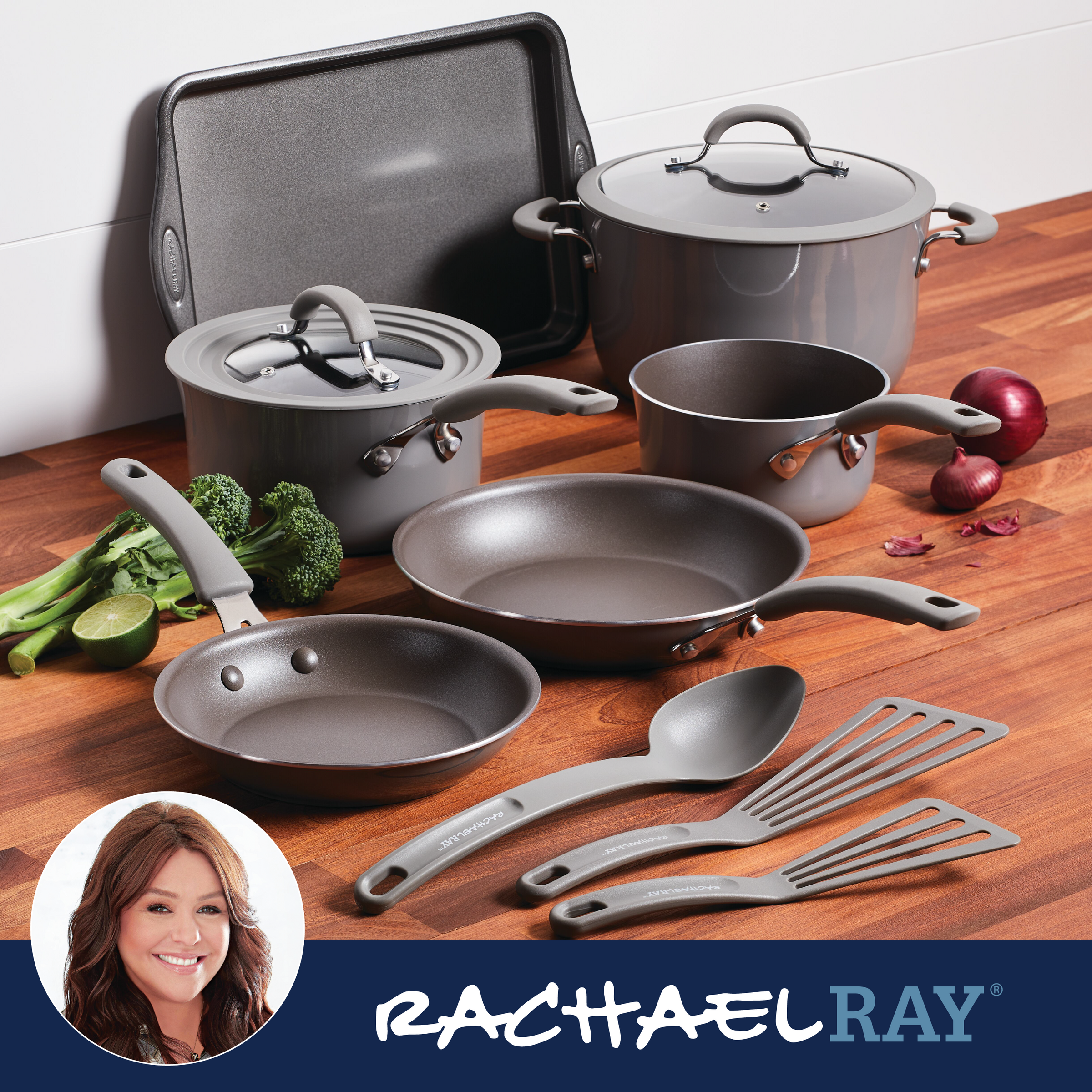 Cookware set with pots, pans, utensils, and vegetables on a wooden surface.