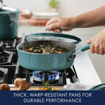 Hands lifting a lid from a steaming teal pan on a gas stove.