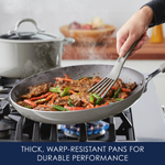 Person cooking steak and vegetables in a gray pan on a gas stovetop.