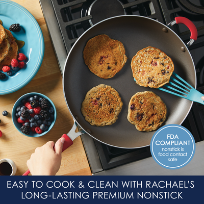 Four pancakes cooking in a nonstick pan on a stovetop, with berries on a plate.