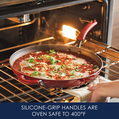 Red pan with tomato dish in oven; silicone-grip handles withstand 400°F.