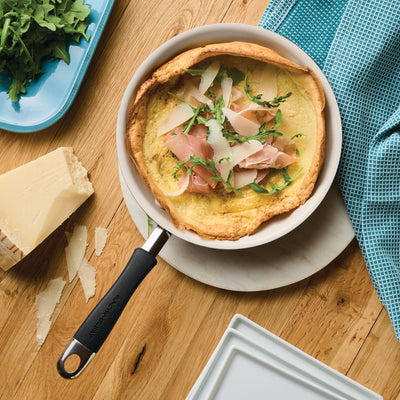 Omelette with prosciutto and arugula in a frying pan on a wooden table.