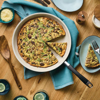 A vegetable frittata in a pan with a slice on a plate beside it.
