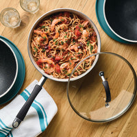 Shrimp pasta in a pan with a glass lid on a wooden table.