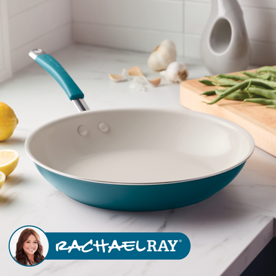 A teal frying pan on a kitchen counter with vegetables and spices.