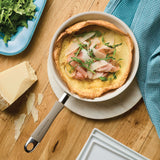 Omelette in a pan topped with ham, cheese, and arugula on a wooden table.