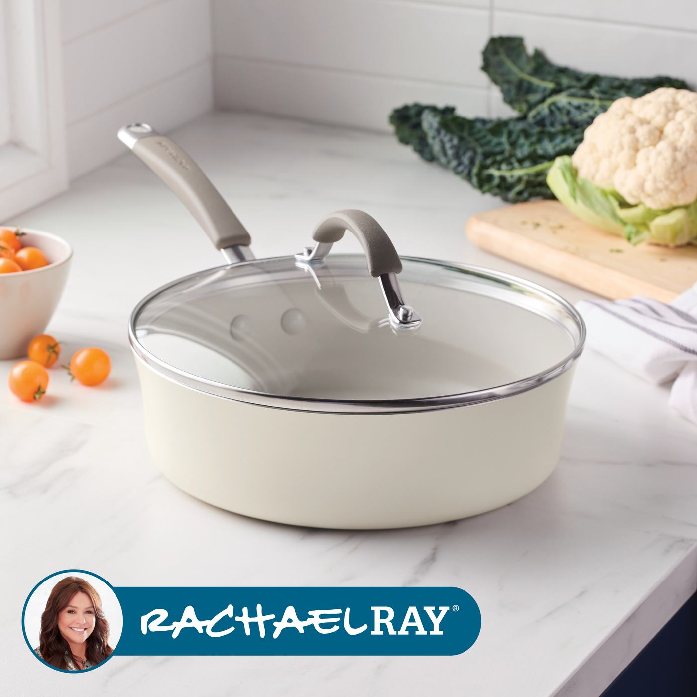 A skillet with a glass lid is on a countertop beside vegetables.