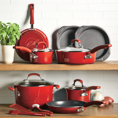 Red cookware set displayed on wooden shelves with basil and vegetables.