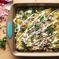 Baked enchiladas with cheese, sauce, onions, and cilantro in a square pan.