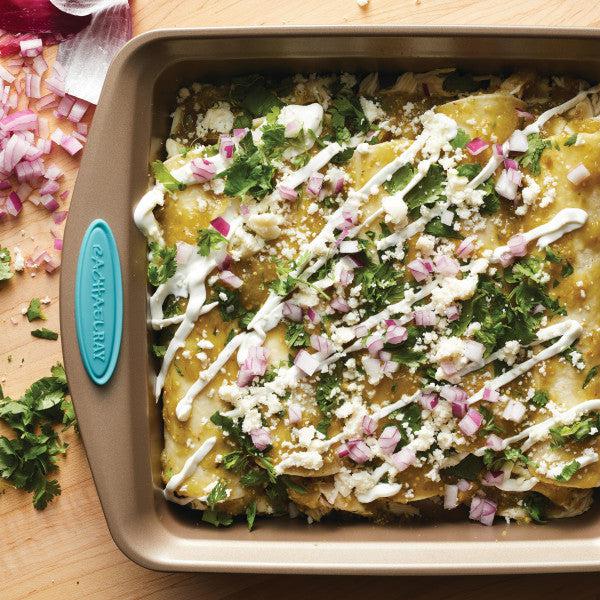 Baked enchiladas with cheese, sauce, onions, and cilantro in a square pan.