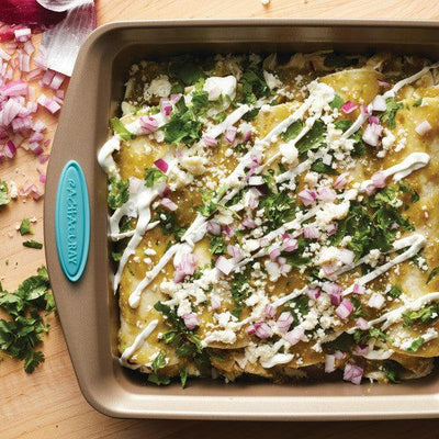 Baked enchiladas with cheese, sauce, onions, and cilantro in a square pan.