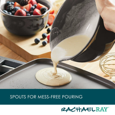 Pouring batter onto a griddle with bowls of fruit in the background.