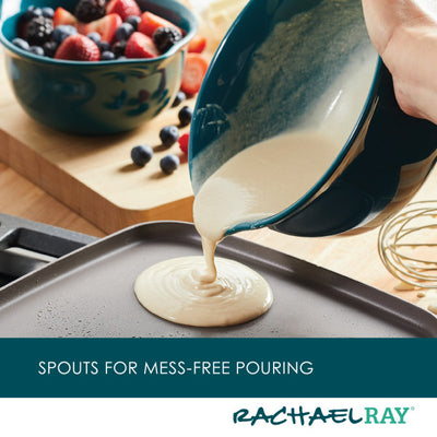 Pouring batter onto a griddle with a bowl, fruit in the background.