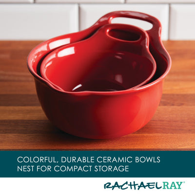 Red nesting ceramic bowls with handles on a wooden surface.