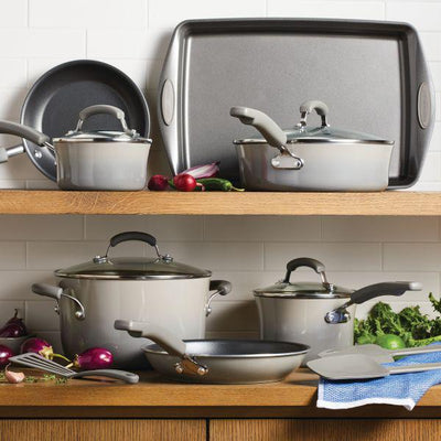 Grey cookware set displayed on wooden shelves with vegetables and linens.