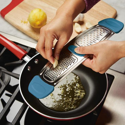 Grating garlic into a frying pan on a stove with a lemon in the background.