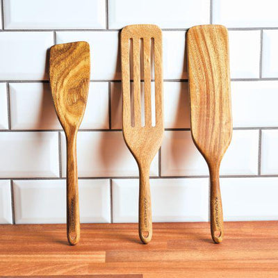 Three wooden spatulas leaning against a white tile backsplash.