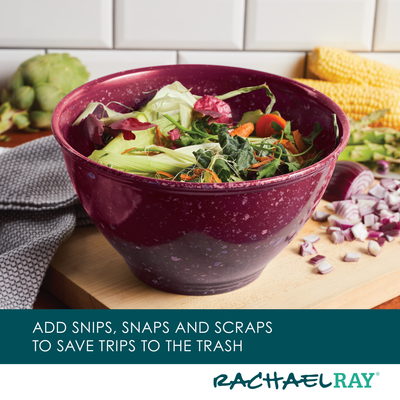 A maroon bowl of vegetable scraps on a kitchen counter with a dish towel.