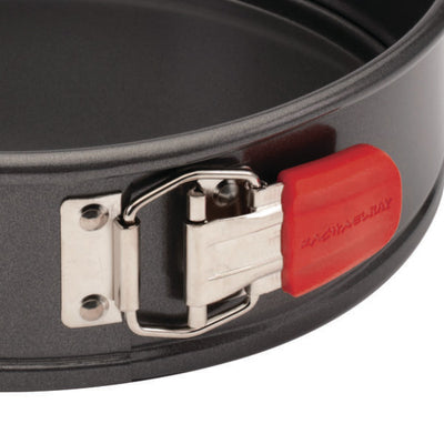 Close-up of a springform pan latch with a red silicone grip.