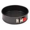 The 9-Inch Nonstick Springform Pan is designed with a black round shape, crafted from heavy gauge steel, and includes a red latch on the side to facilitate easy food release.