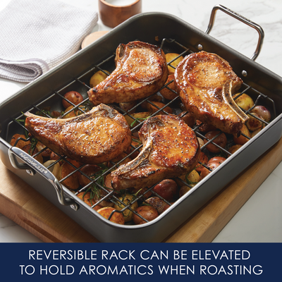 Pork chops roasting on a reversible rack over seasoned vegetables in a pan.