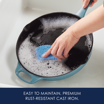 Person cleaning a cast iron pan with a sponge and soapy water.