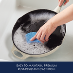 Hand cleaning a cast iron pan with a blue sponge in soapy water.