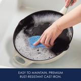 Hand cleaning a cast iron pan with a blue sponge in soapy water.