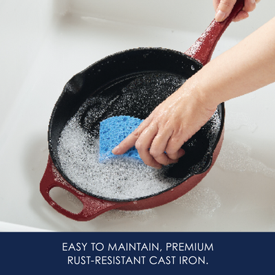 Hand cleaning a cast iron pan with a blue sponge in soapy water.