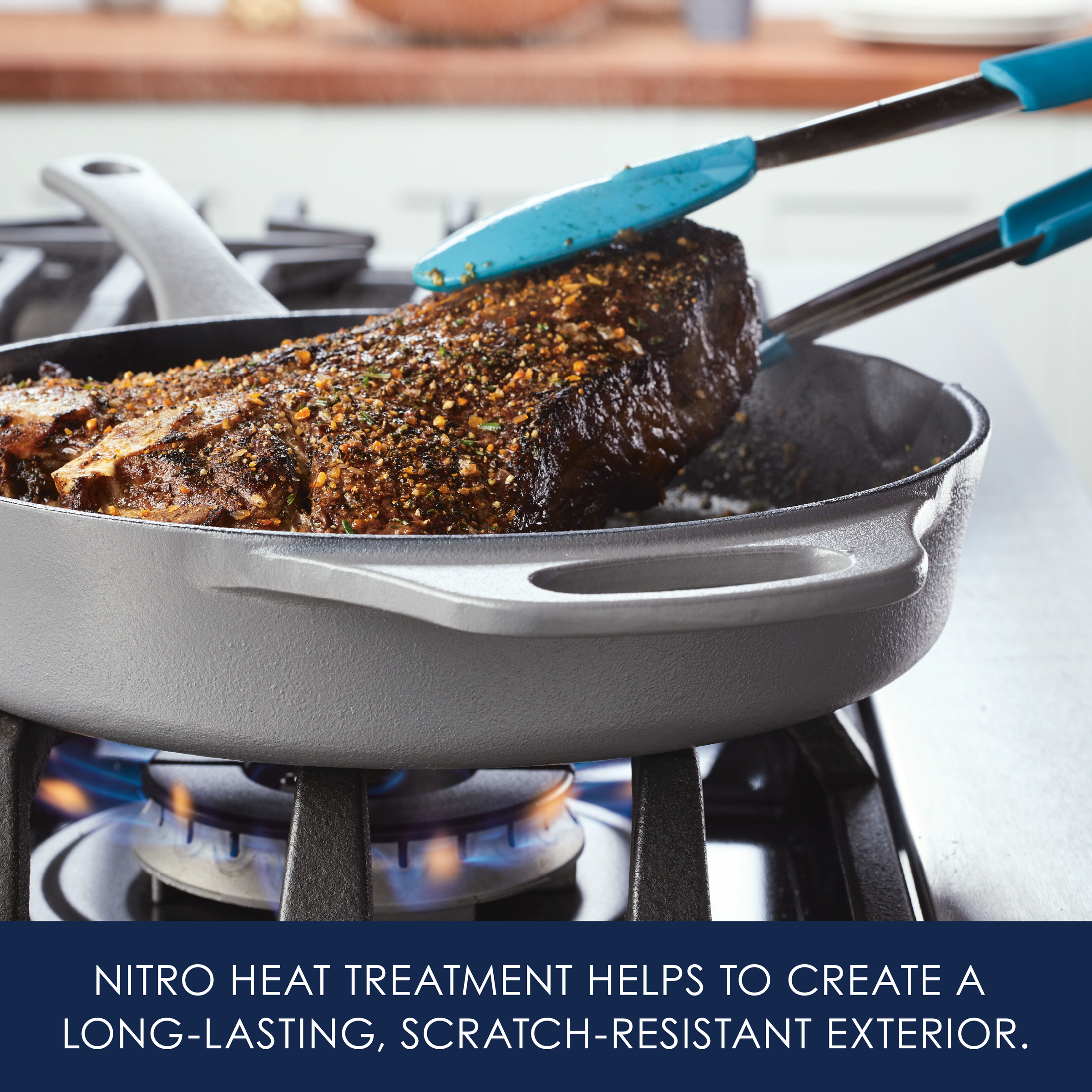 A steak being cooked in a skillet with blue tongs holding the meat.