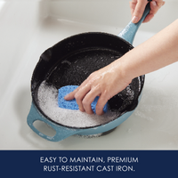 Hand scrubbing a blue cast iron pan with soap in a sink.