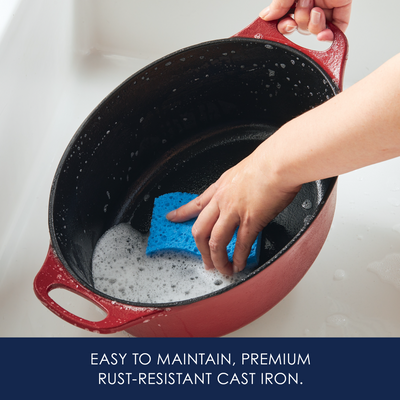 Hand cleaning a red cast iron pot with a blue sponge and soap.