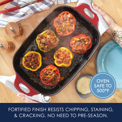 Stuffed peppers in a red pan on a wooden table with a blue plate nearby.