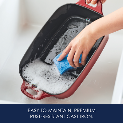 Person scrubbing a cast iron pan with a blue sponge in a sink.