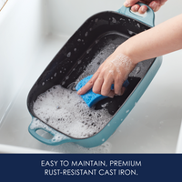 Hand scrubbing a cast iron pan with soap and a blue sponge in a sink.