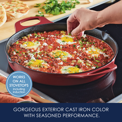 Red cast iron pan with eggs and tomato sauce on a stovetop.
