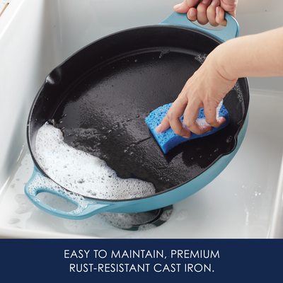 Person cleaning a cast iron pan with a sponge in a sink.