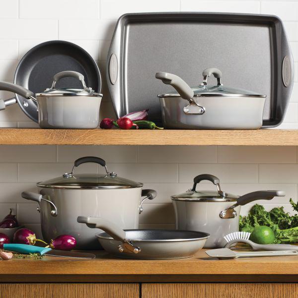 Shelves in the kitchen featuring Classic Brights Nonstick Cookware Sets, along with onions and leafy greens.