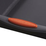 Close-up of a black baking sheet with an orange handle grip.