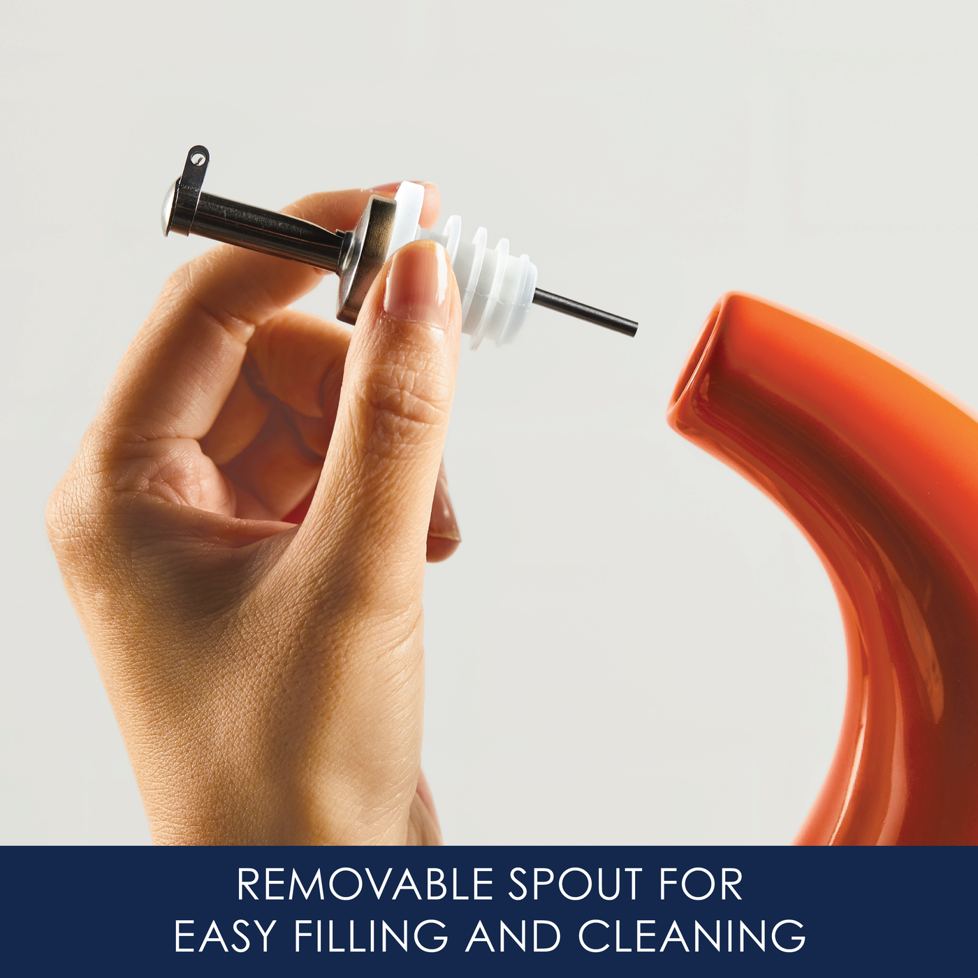 Hand holding a removable spout near an orange container.