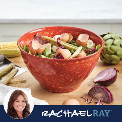 Red bowl with onions and eggshells beside corn and artichoke on a countertop.