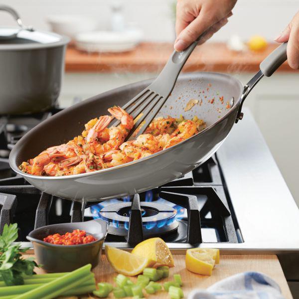 A person is skillfully cooking shrimp and vegetables in a Cook + Create Nonstick Frying Pan on the stove.
