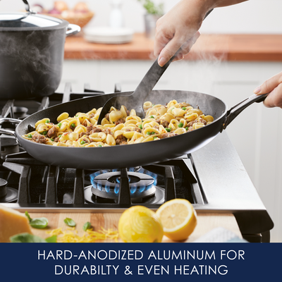 Pasta cooking in a black pan on a stove with lemons nearby.